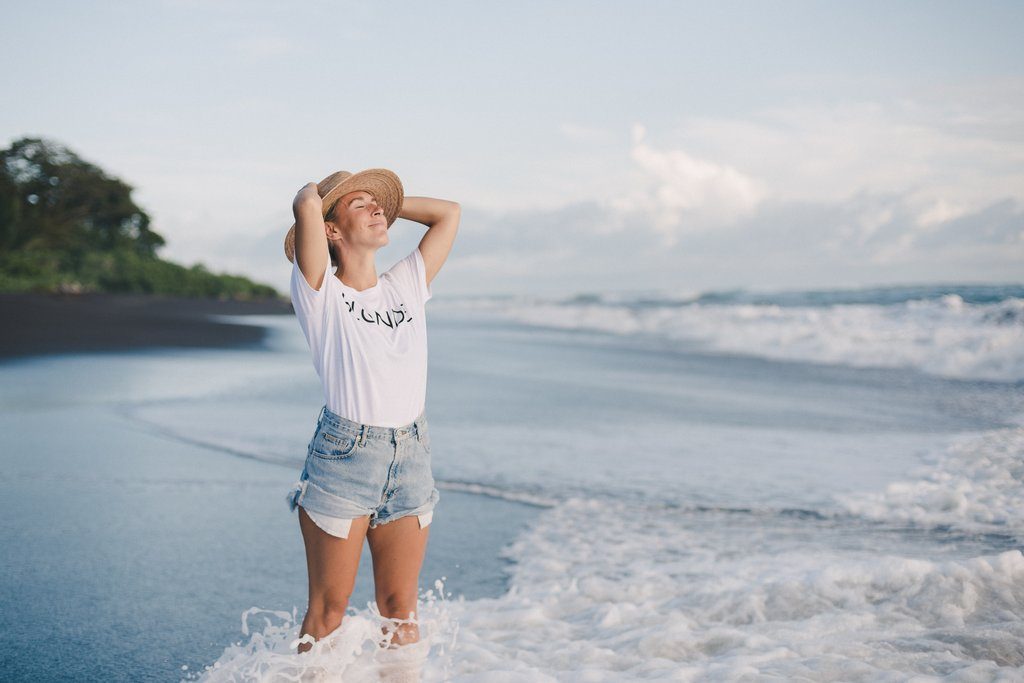 Ally Maz photographed standing in the ocean as the looks to the sky wearing a white Brunette the Label tshirt.