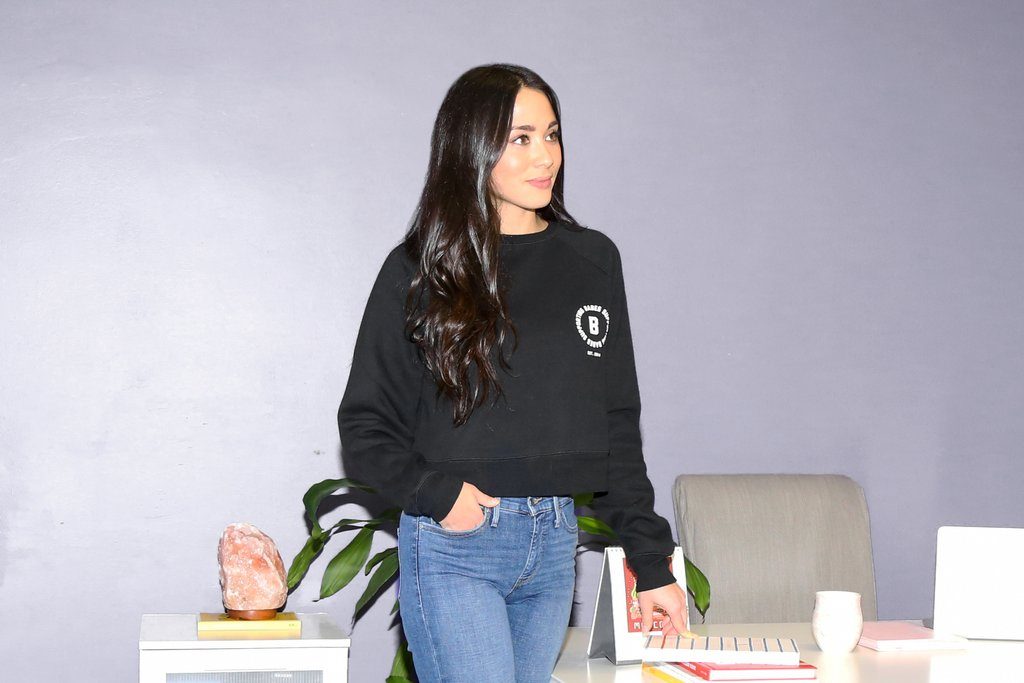 Shnane Liem Abbrusci of Vive Social photographed sitting on a stairs in a Brunette the Label sweatshirt.
